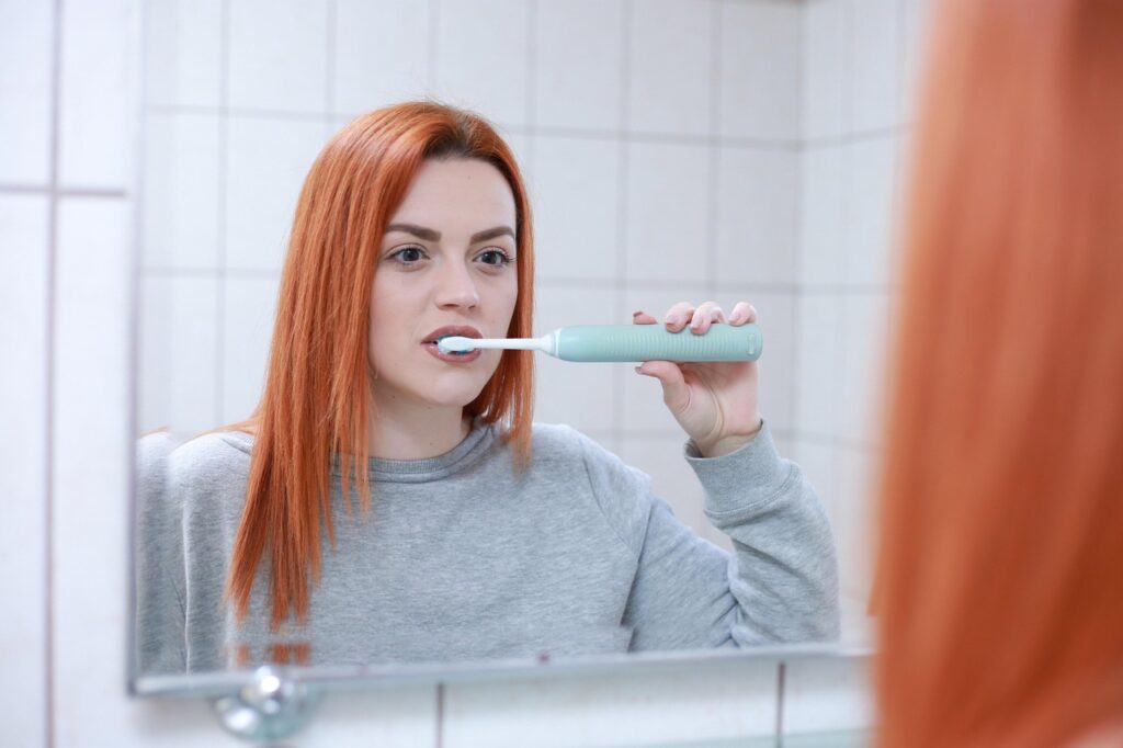 Una joven se mira en un espejo mientras se cepilla los dientes con un cepillo eléctrico
